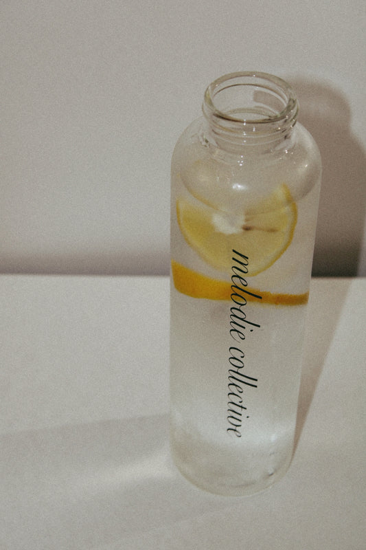 Clear bottle with lemon slices and 'Melodic Collective' branding on a white background