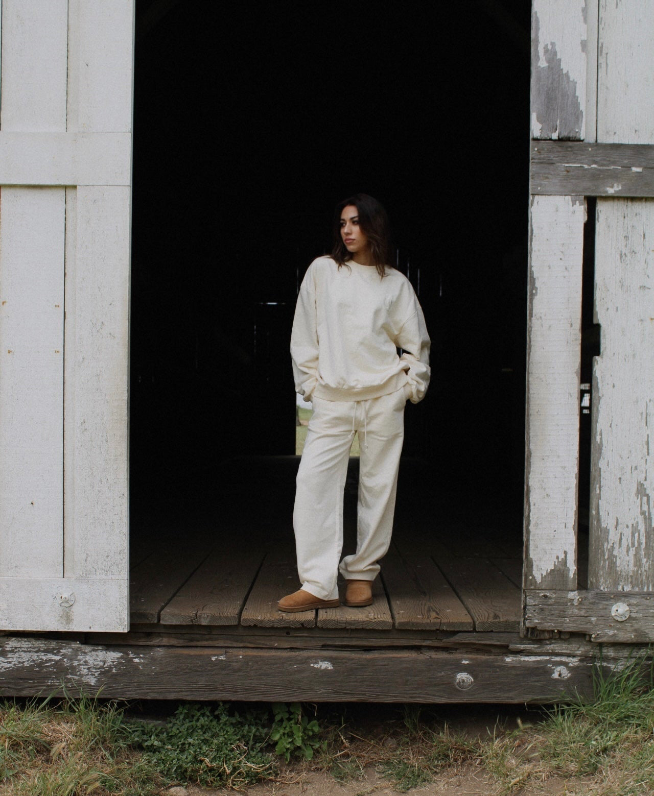 Person in cream outfit standing in a dark doorway of an old wooden building