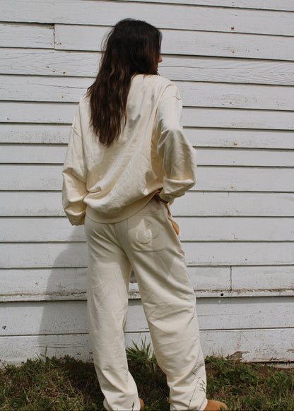 Person wearing a cream-colored outfit standing against a white wall.